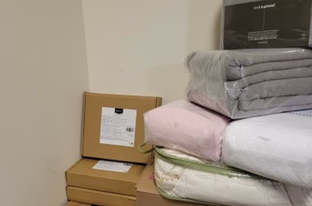 Stacks of bed sheets, kitchen supplies, and other boxes of donations.